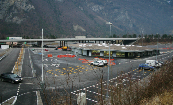 Blick auf das Schwerverkehrskontrollzentrum. Im Vordergrund PW-Parkplätze, in der Bildmitte das Verwaltungsgebäude. Im Hintergrund führt eine Brücke über das Gelände.